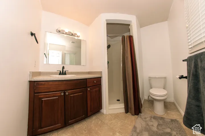 Bathroom featuring a wood-finish vanity with a light-toned countertop, an integrated sink, a rectangular mirror, and a standing shower with a curved enclosure