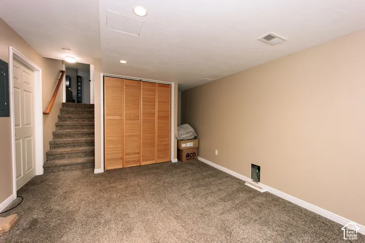 Carpeted flooring, neutral wall paint, recessed ceiling lighting, wood-finish bi-fold closet doors, and a carpeted staircase with wood handrail
