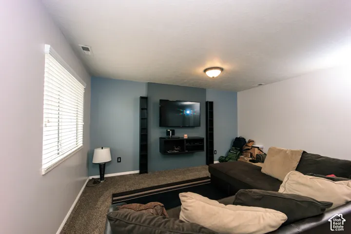 Wall-mounted media console, recessed ceiling light, window with horizontal blinds, textured carpet, and a flush-mount ceiling fixture