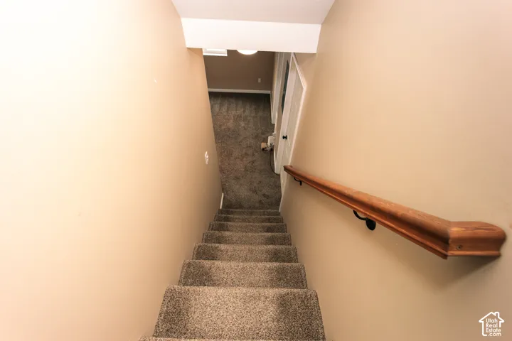 Carpeted staircase with a wood handrail and neutral wall finishes