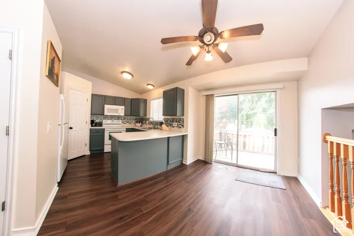 Vaulted ceiling kitchen featuring wood-finish flooring, white appliances, a sliding glass door, and a built-in kitchen island with countertop