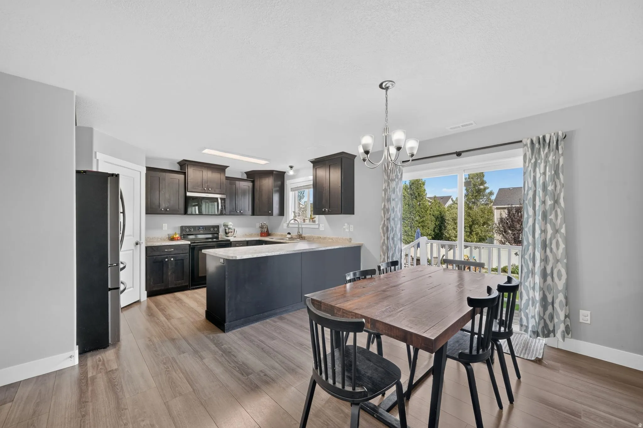 Open-concept kitchen and dining area featuring dark wood cabinetry, light-toned countertops, and wood-finish flooring