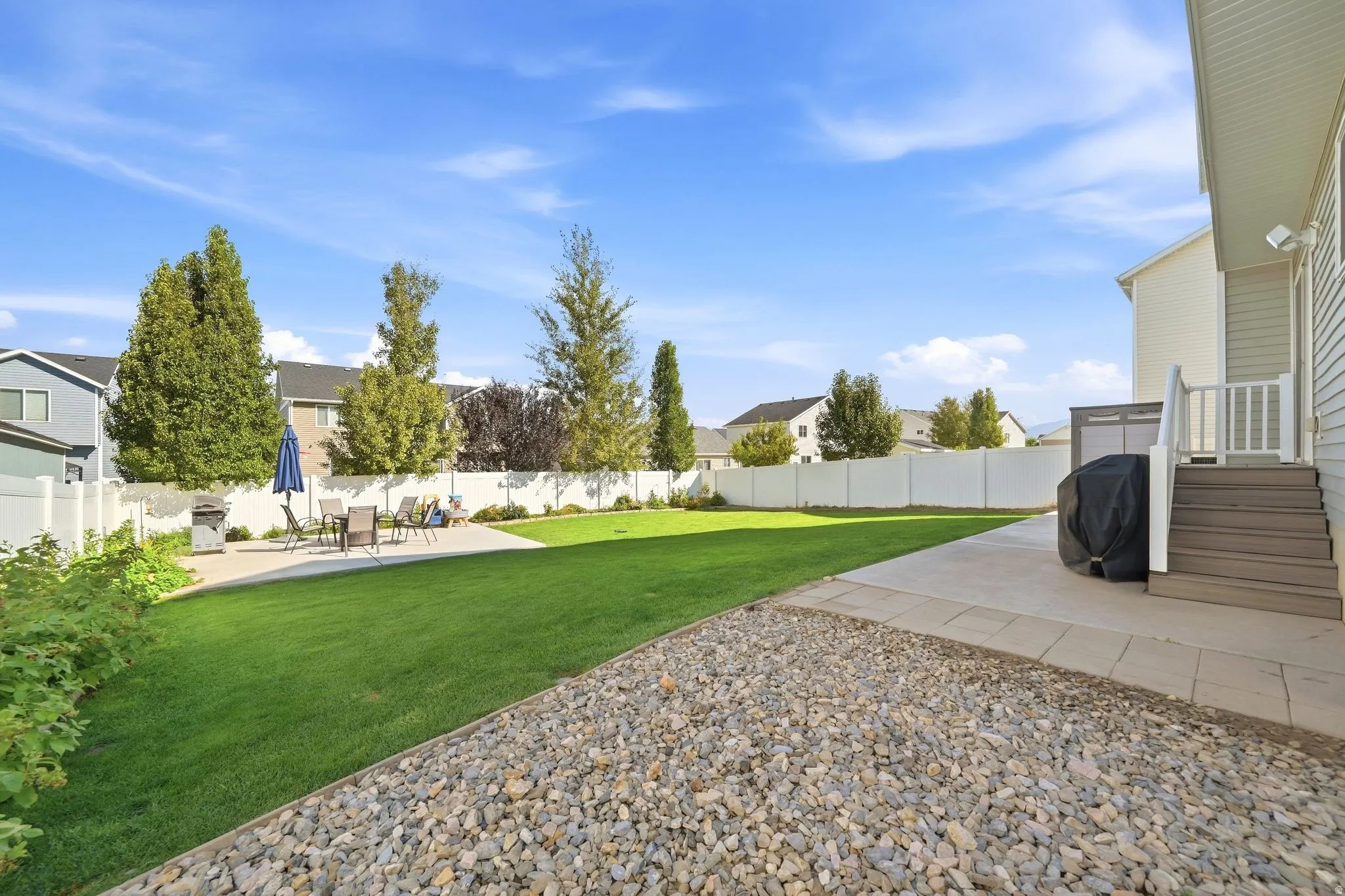 Expansive backyard featuring a manicured lawn, concrete patio, and white vinyl fencing