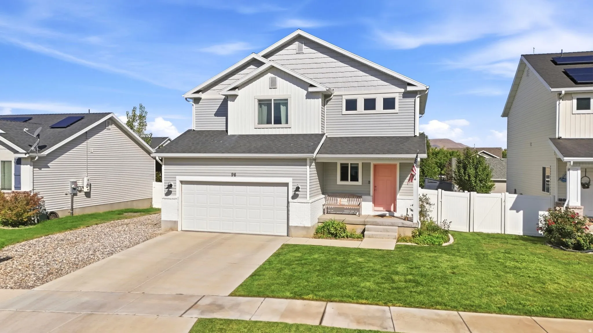 Two-story residence featuring light gray siding with white trim accents, an attached two-car garage, a concrete driveway, a front porch with an accent door, and a fenced yard