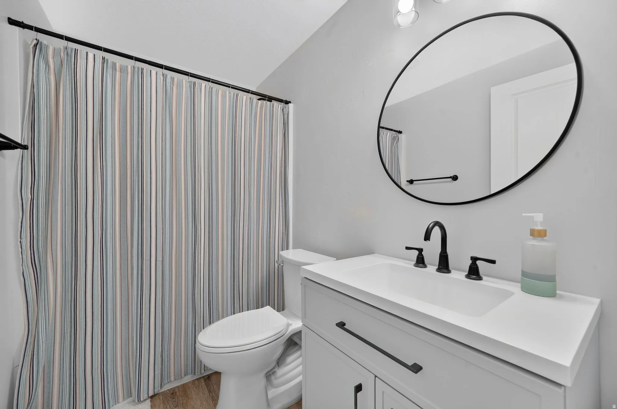 White vanity with a rectangular undermount sink, matte black faucet, and a round black-framed mirror