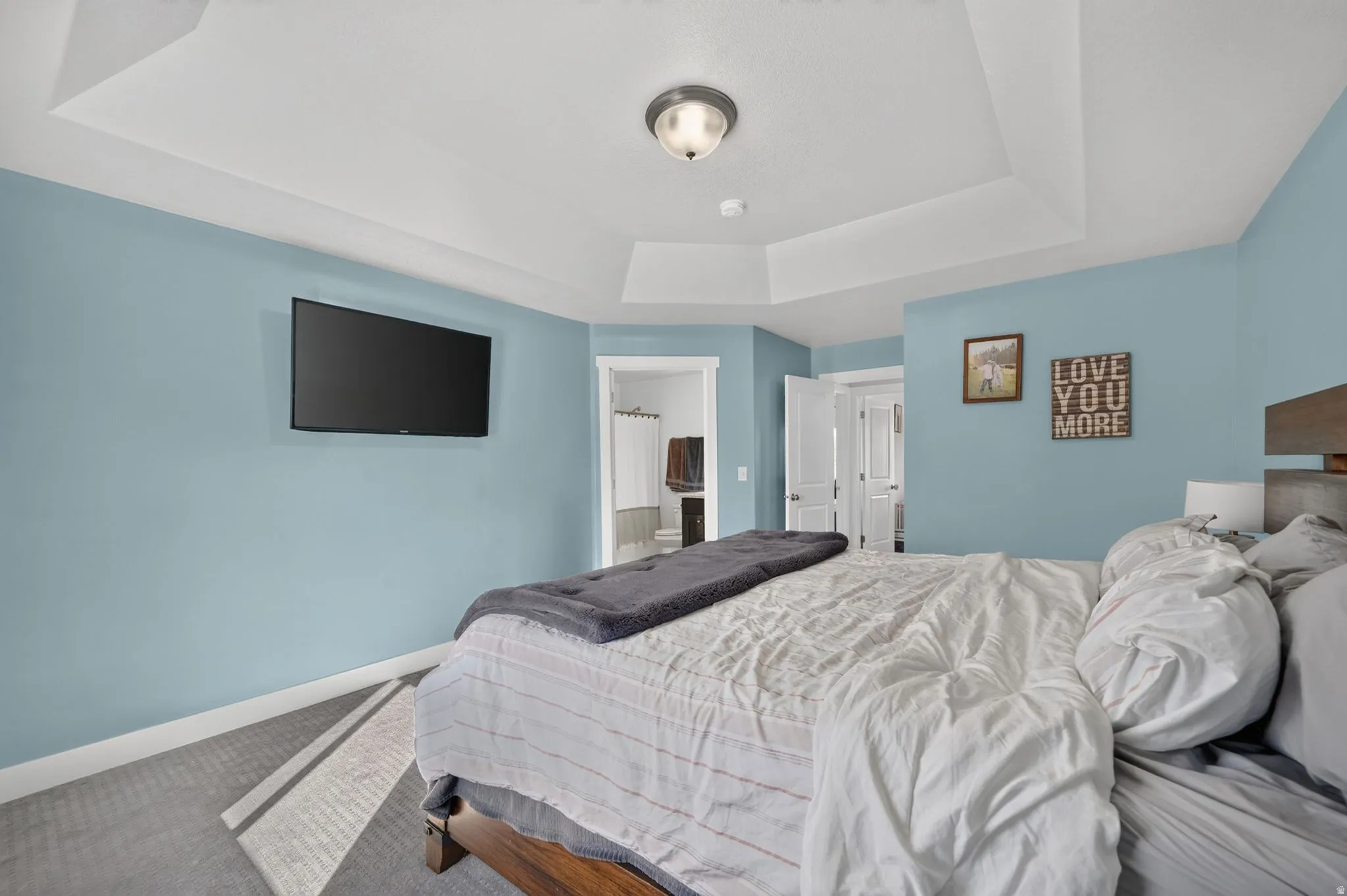 Tray ceiling with recessed lighting, light blue wall paint, carpet flooring with geometric pattern, white trim, and a white interior door