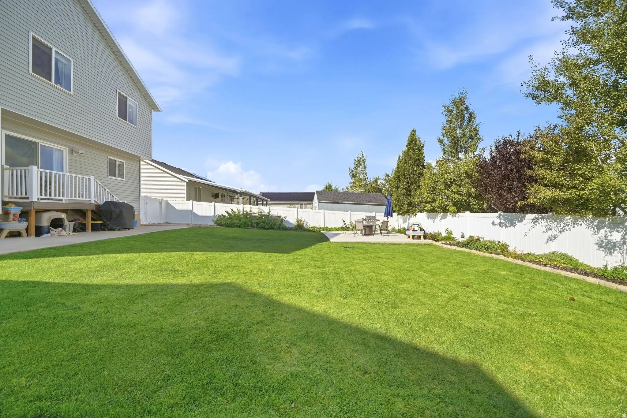 Expansive green lawn with a privacy fence, concrete patio, and mature landscaping