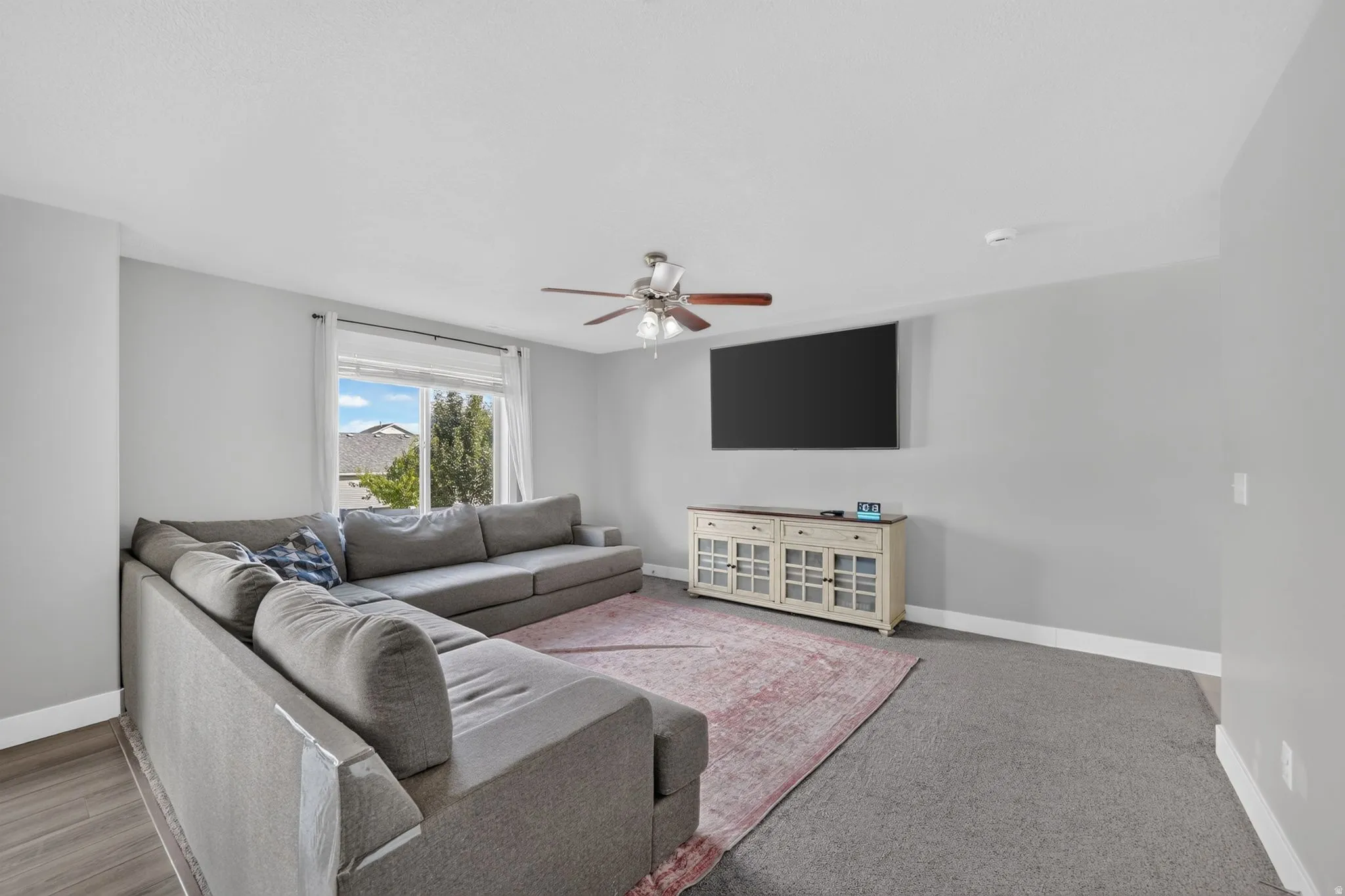 Recessed window with white trim, ceiling fan with wood-finish blades, light gray walls, and varied flooring