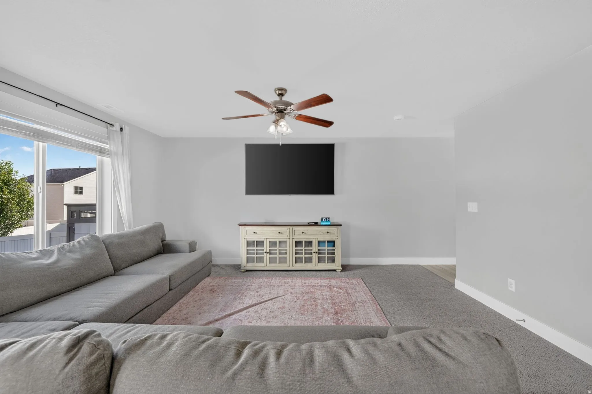 Large picture window, ceiling fan, recessed lighting, wall-mounted television, and a built-in media console