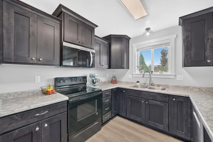 Kitchen featuring dark wood cabinetry, light-toned countertops, wood-finish flooring, a stainless steel double basin sink, and a black electric range with an overhead microwave