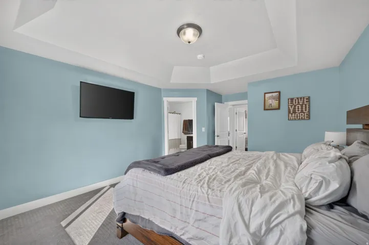 Tray ceiling with recessed lighting, light blue wall paint, carpet flooring with geometric pattern, white trim, and a white interior door