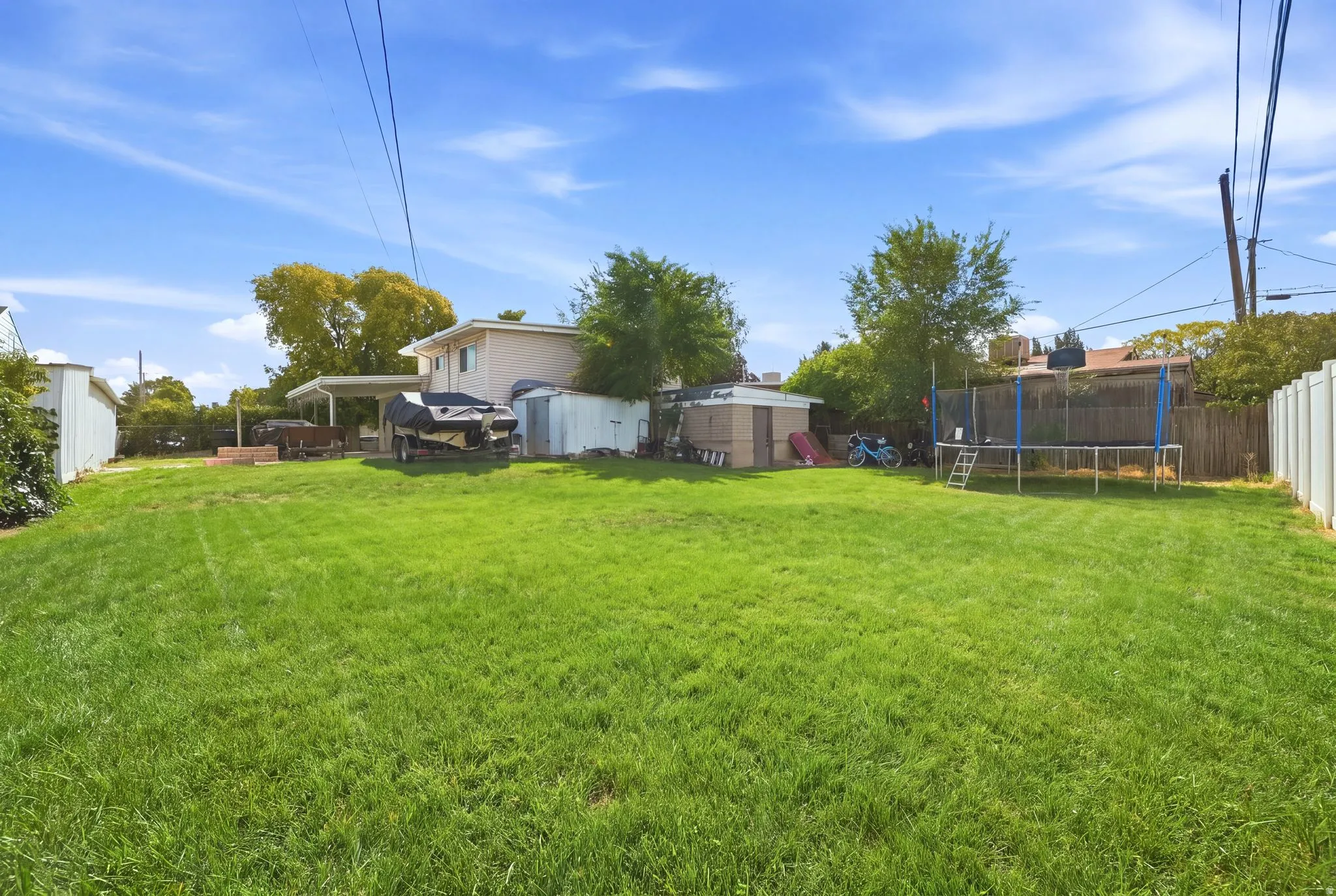 Expansive grassy yard with a privacy fence, an attached carport, and multiple storage sheds