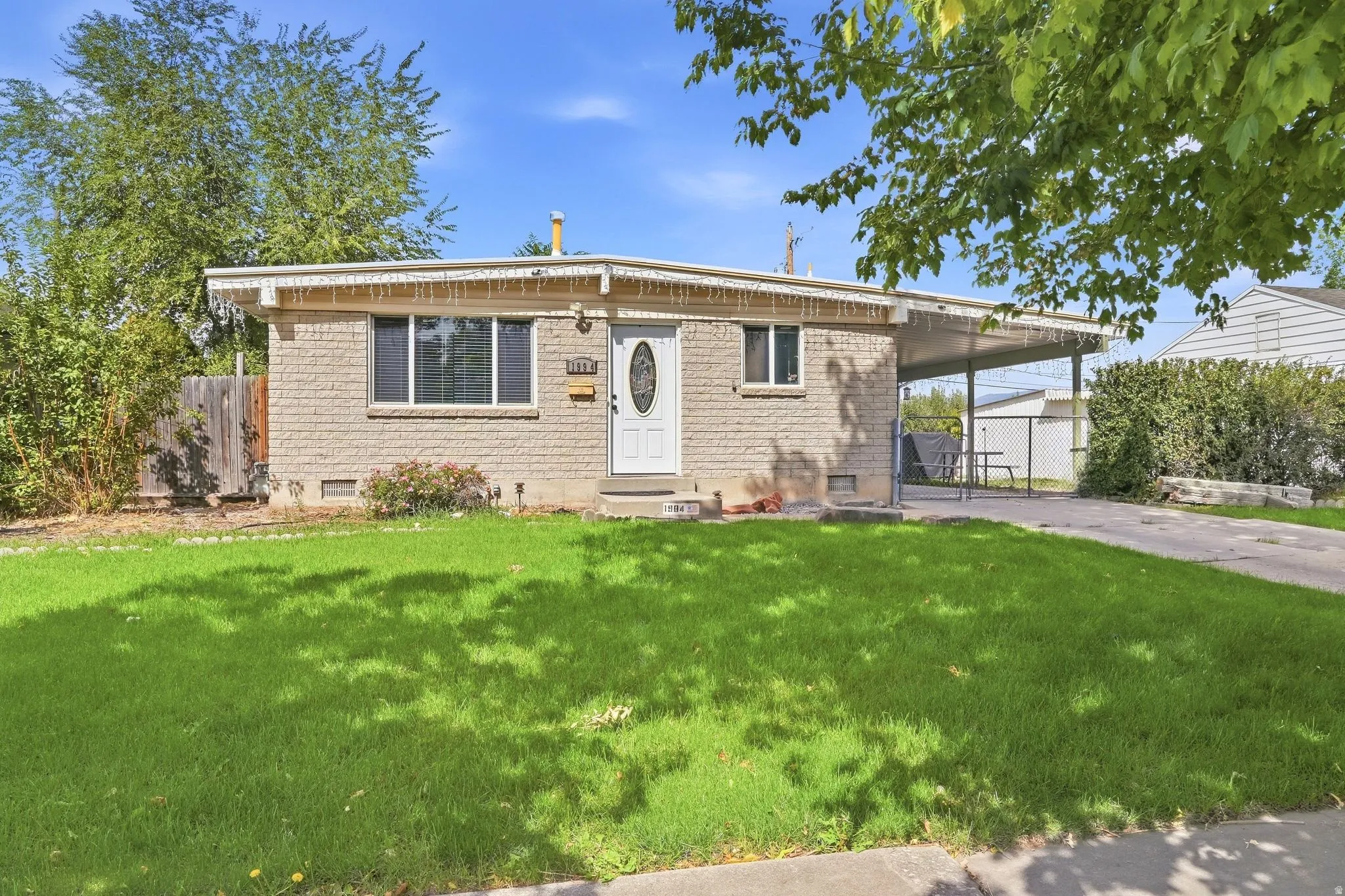 Brick exterior with a white entry door, an attached carport, and a front lawn