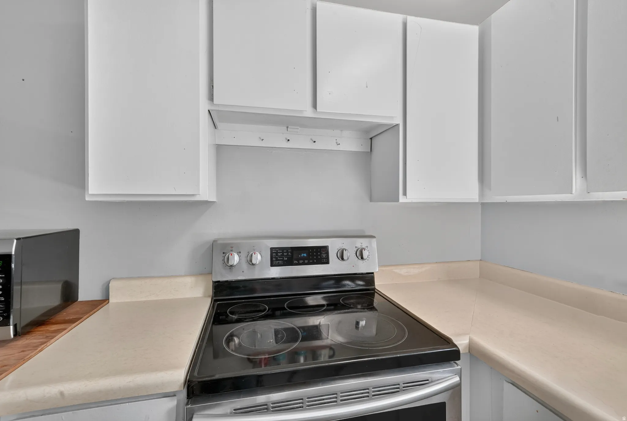 White upper cabinetry, solid surface countertops, and a stainless steel electric range