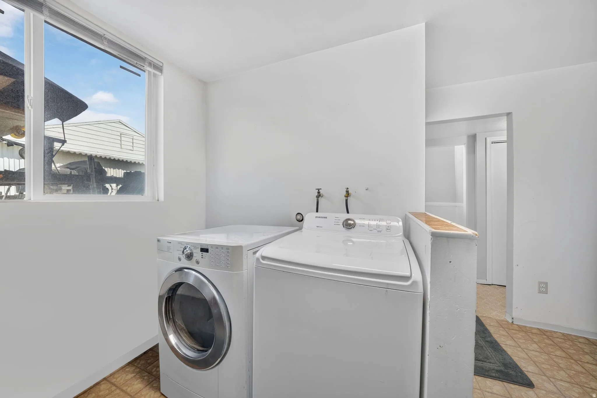 Dedicated laundry area with a window, tile-finish flooring, and a half-wall partition