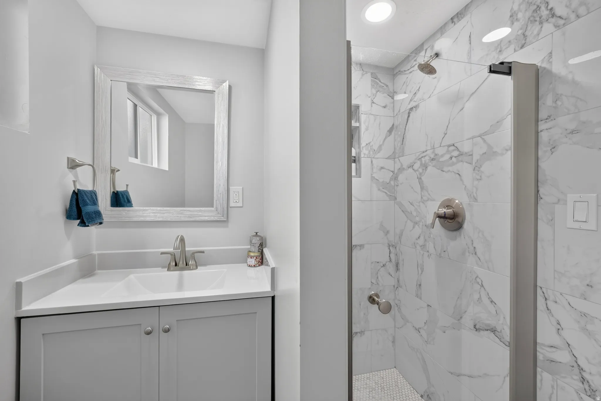 Bathroom featuring a vanity with an integrated sink, framed mirror, and a walk-in shower with floor-to-ceiling tile