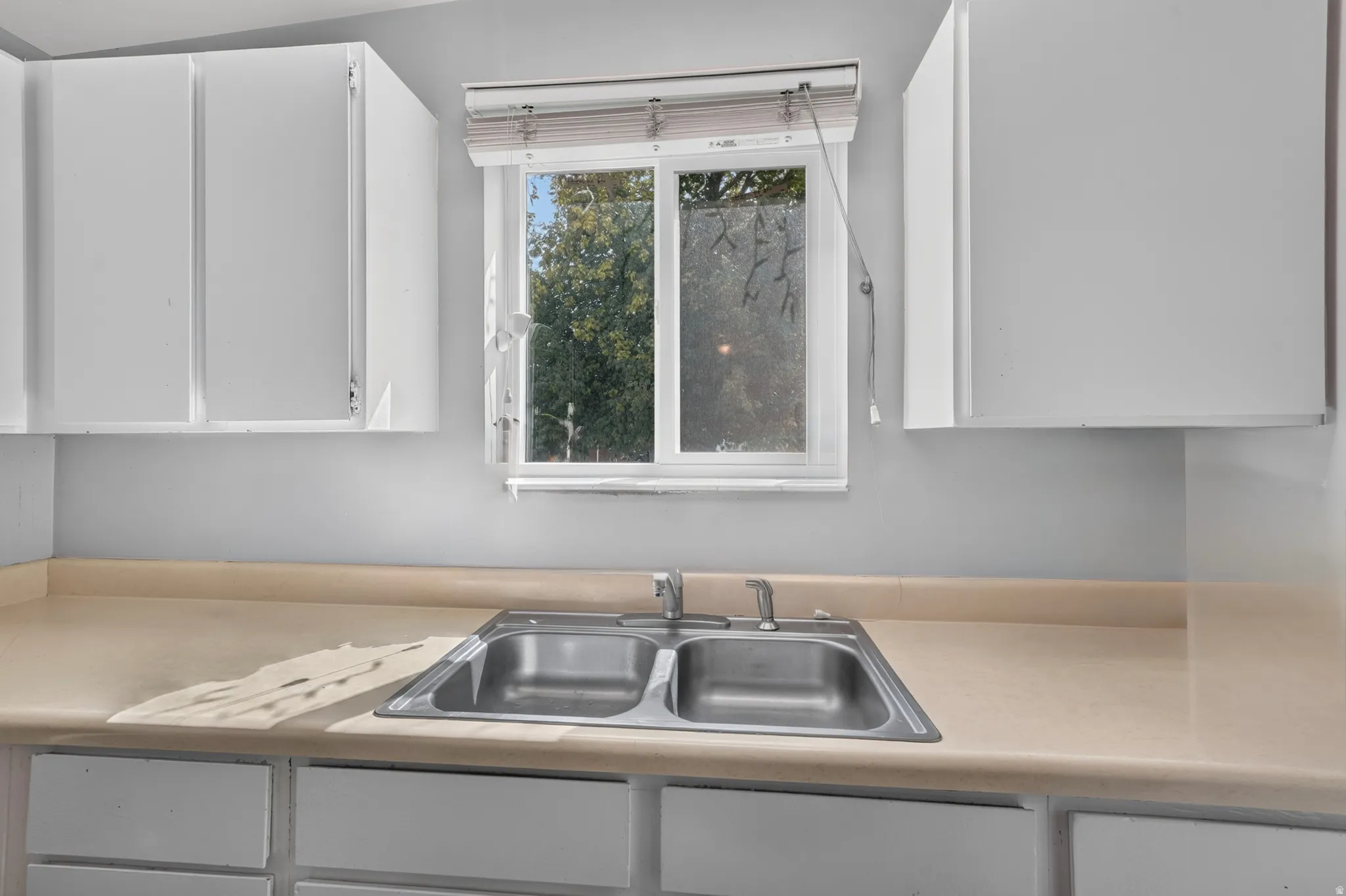 Stainless steel double basin sink set into a laminate countertop, flanked by white upper and lower cabinetry