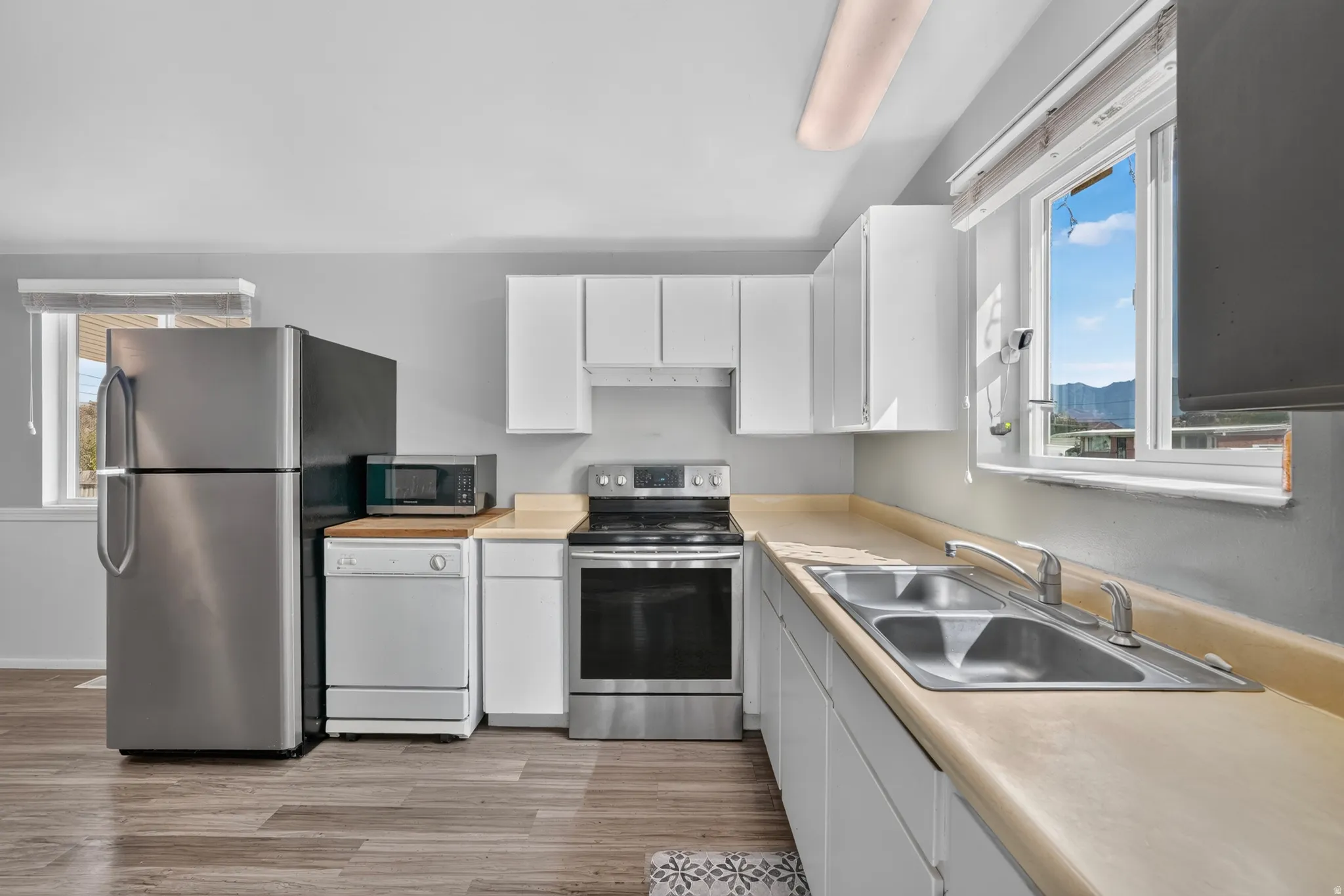 Kitchen featuring wood-finish flooring, white cabinetry, a stainless steel refrigerator, and a double basin sink