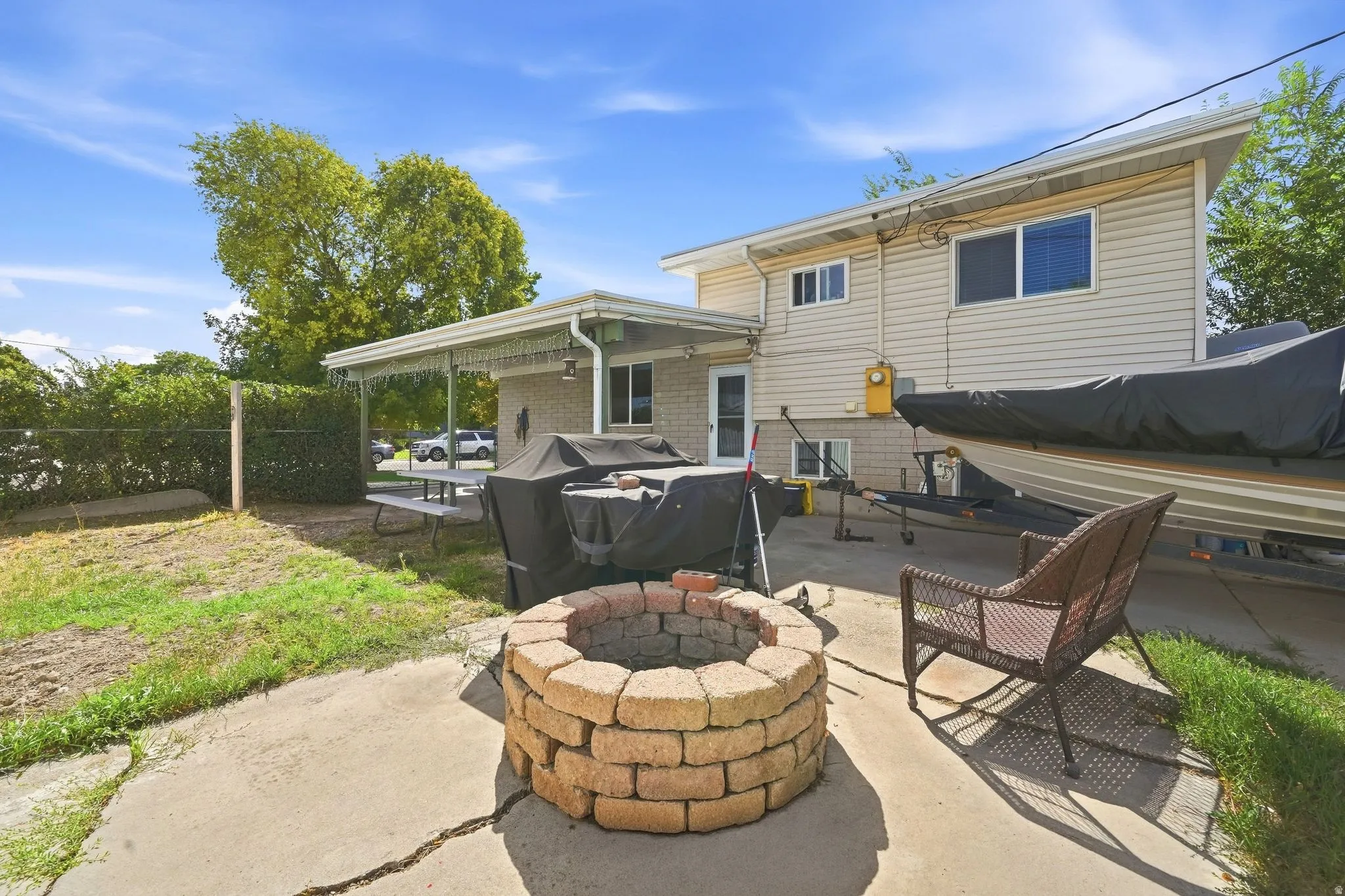 Expansive patio area featuring a built-in fire pit with brick detailing, covered patio, and mature perimeter hedging