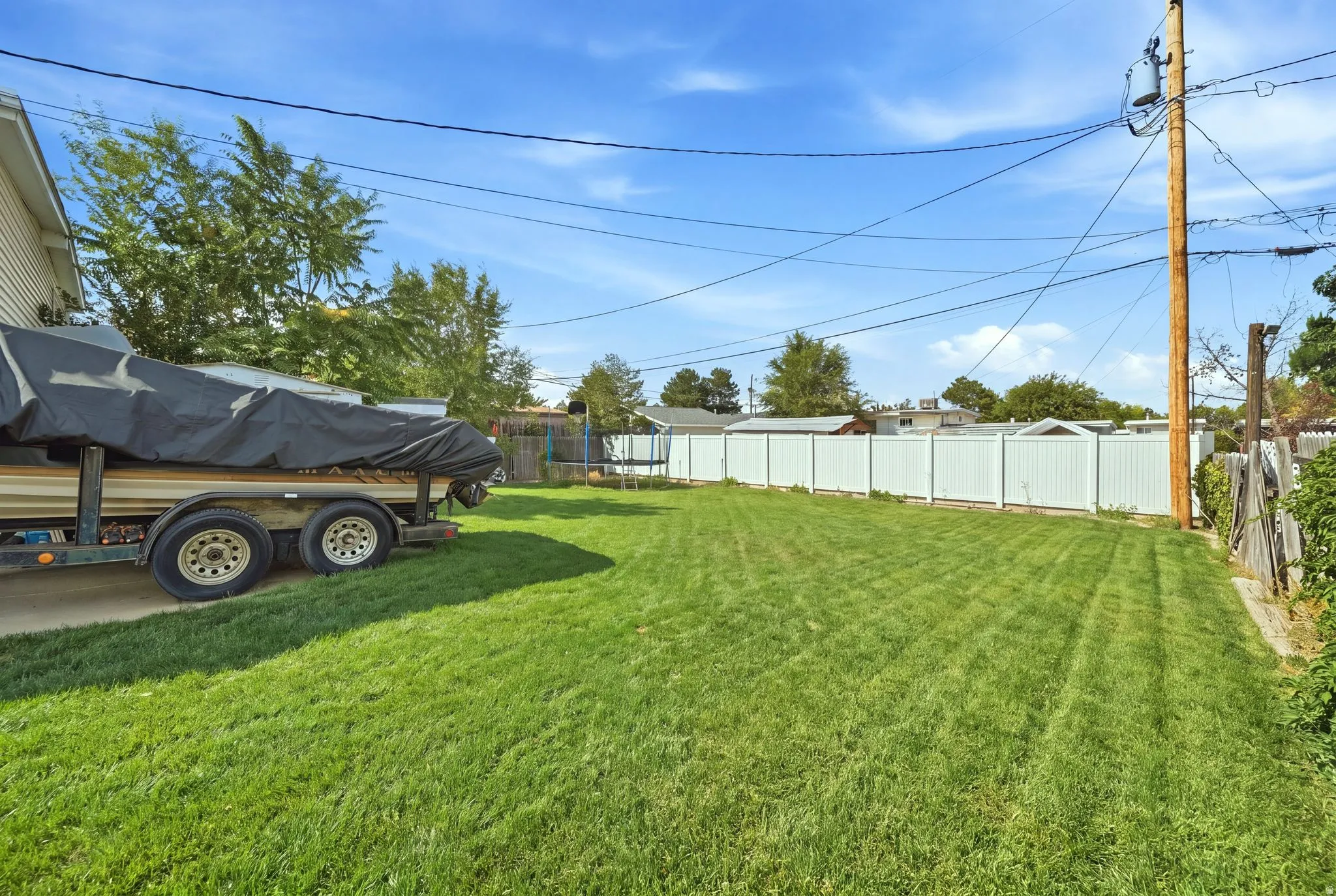 Expansive grassy yard with white privacy fencing and a paved side yard