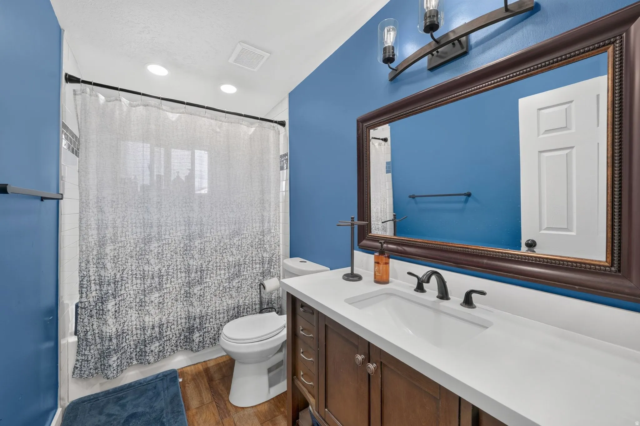 White countertop vanity with wood-finish cabinetry, a drop-in sink, and a dark bronze faucet