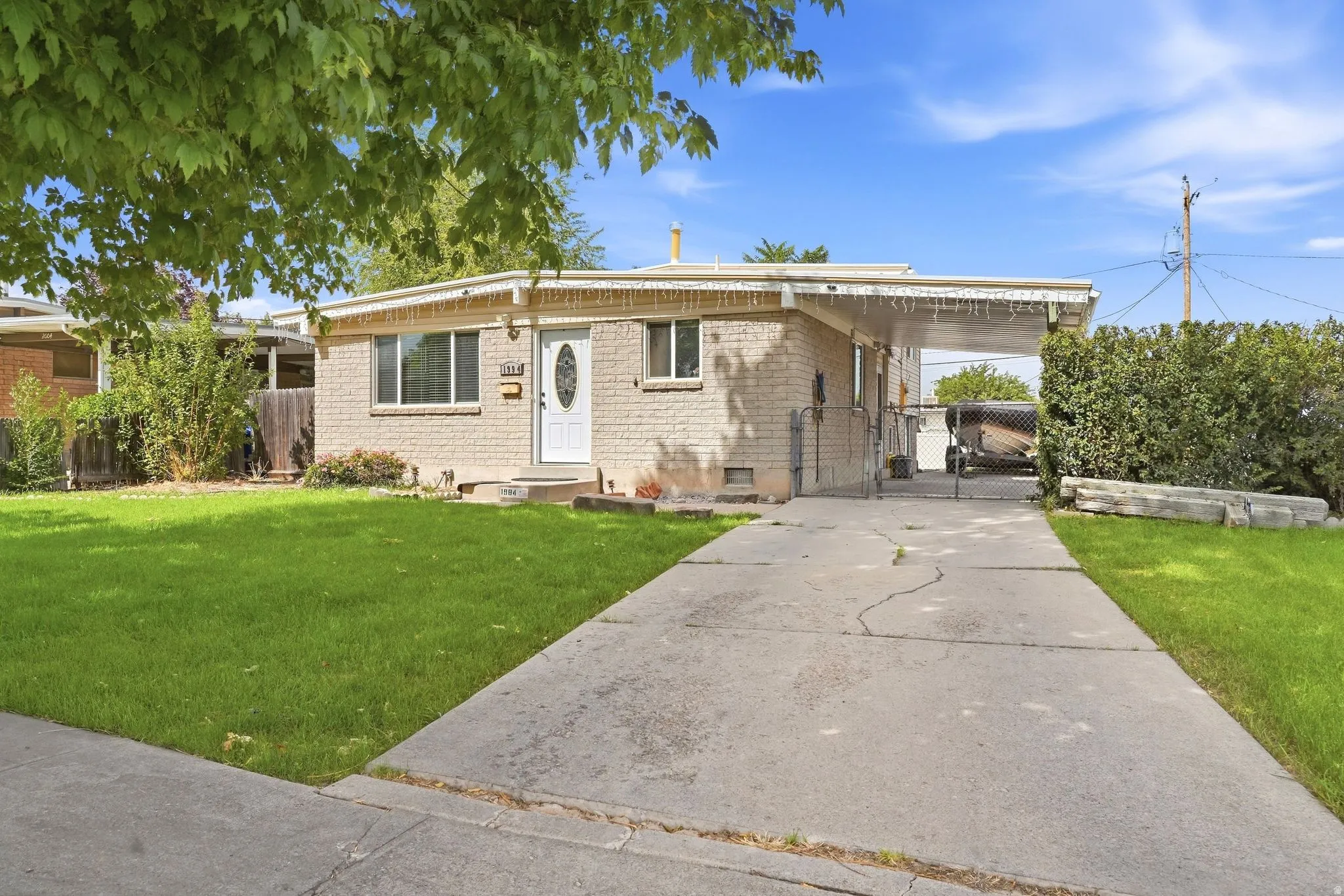 Light brick exterior, covered carport, concrete driveway, and front lawn