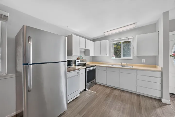 Kitchen featuring wood-finish flooring, white cabinetry, laminate countertops, and stainless steel appliances