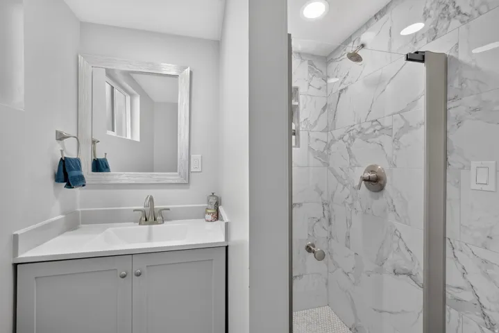 Bathroom featuring a vanity with an integrated sink, framed mirror, and a walk-in shower with floor-to-ceiling tile