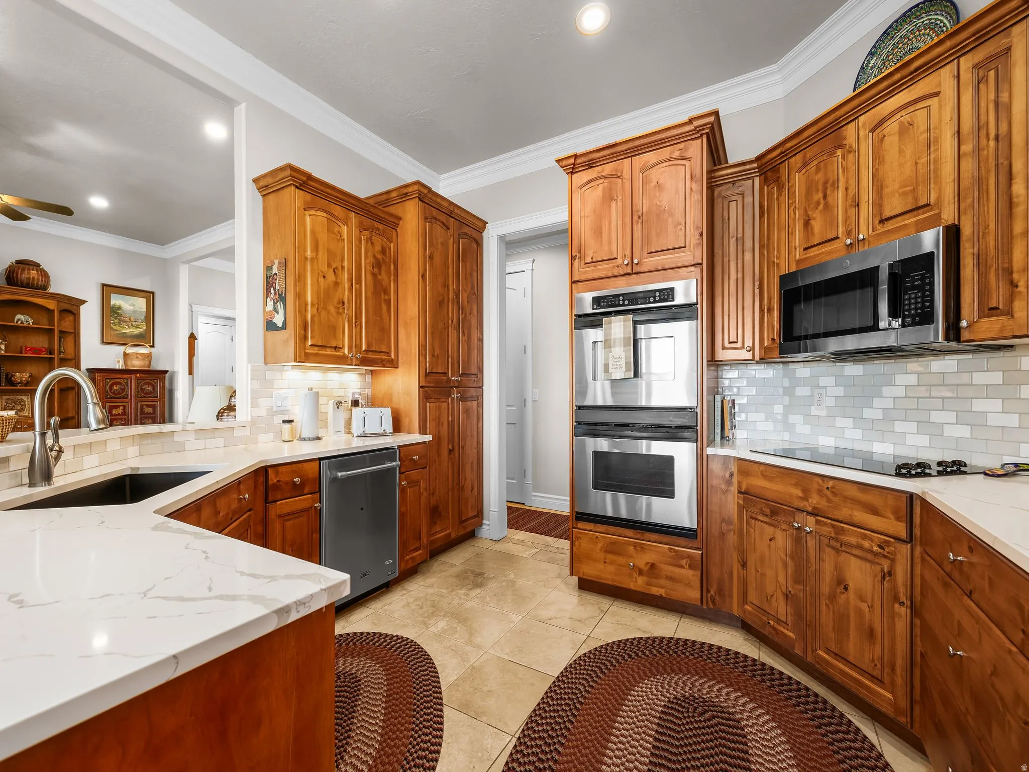 Kitchen featuring wood cabinetry, stainless steel appliances, light-toned countertops, tile flooring, and a subway tile backsplash
