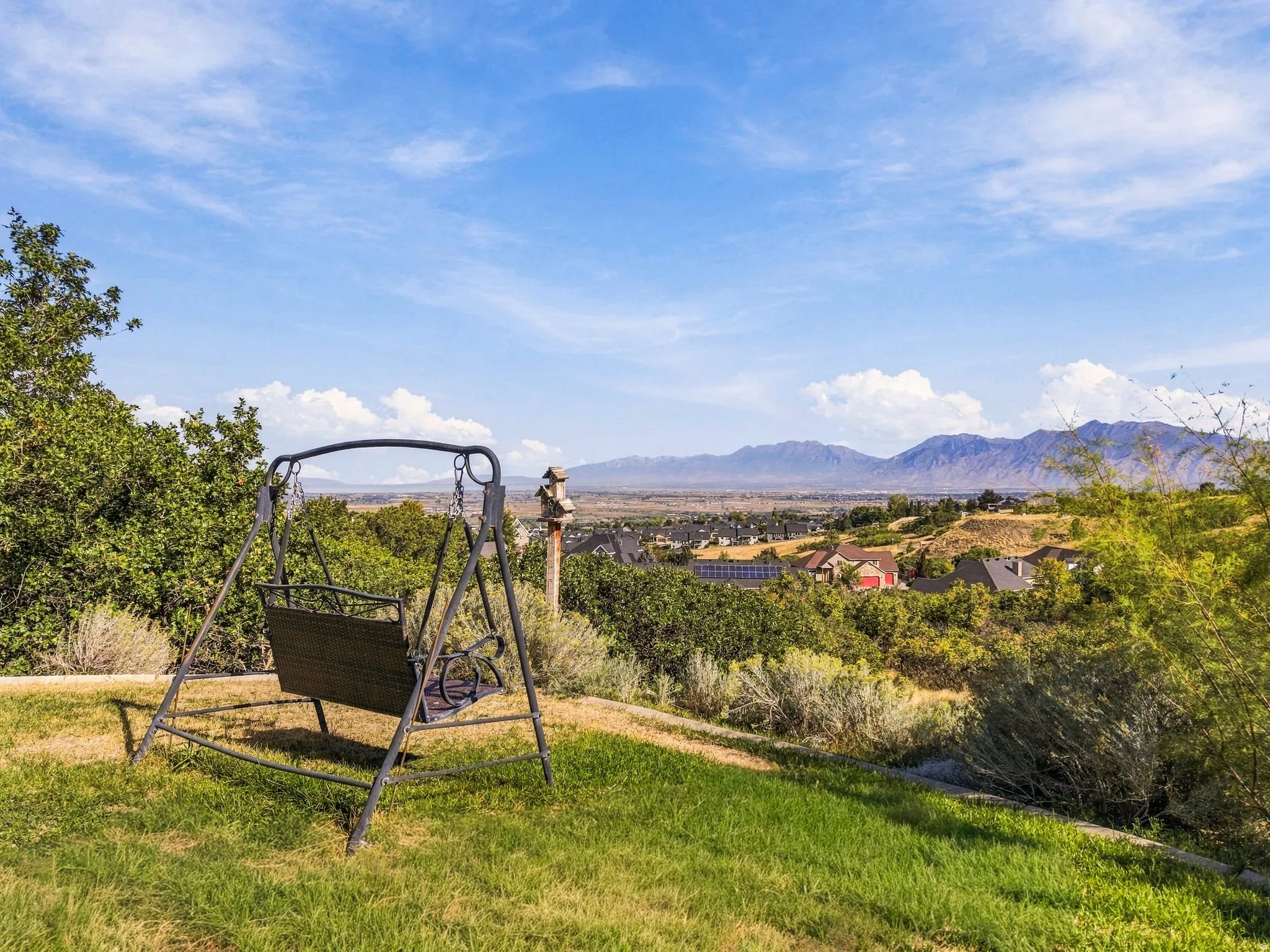 Expansive sloped lawn with mature landscaping, distant mountainous terrain, and a visible neighborhood below