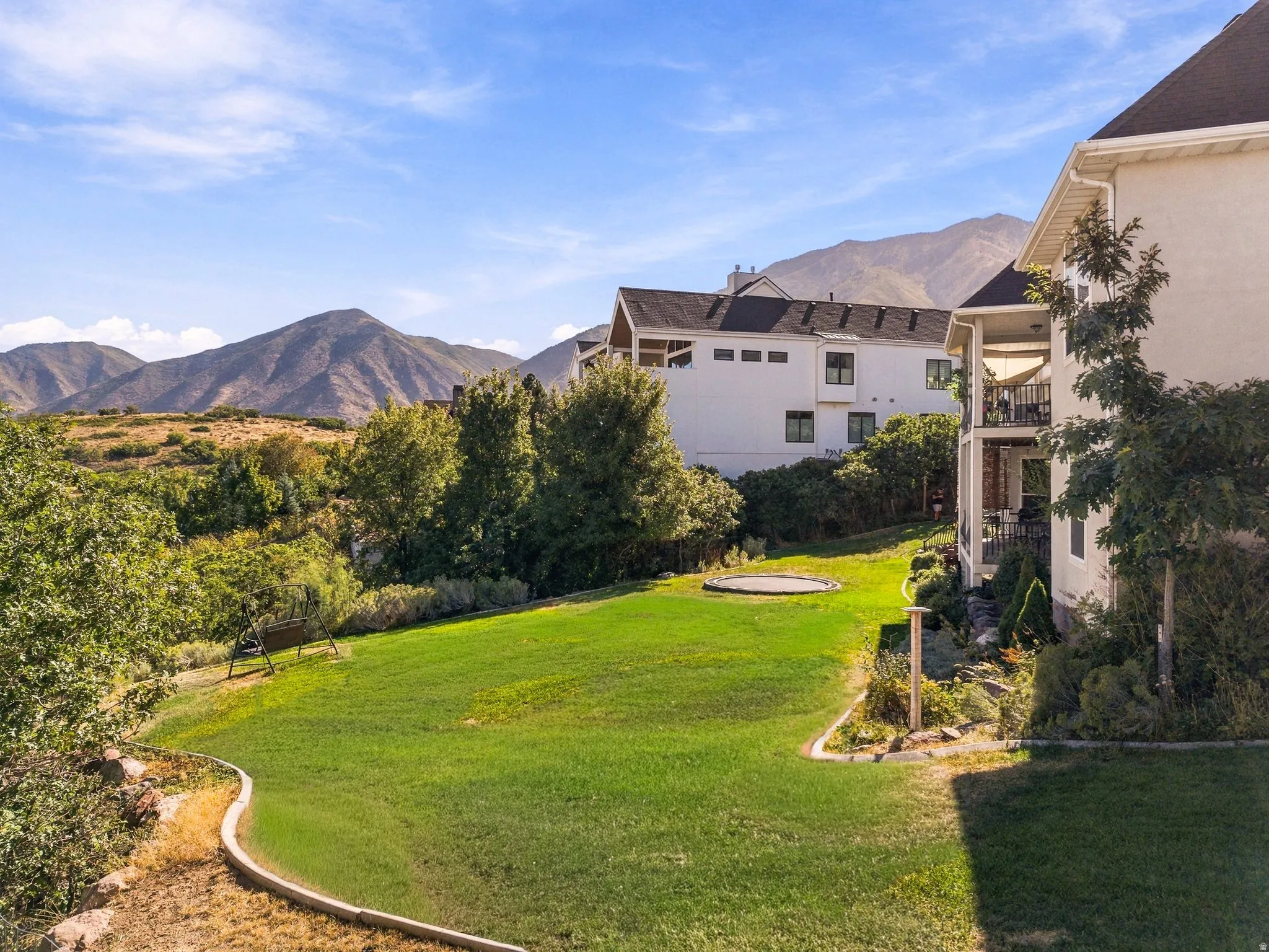 Expansive manicured lawn with a curved landscape border, surrounded by mature trees, and a mountain backdrop