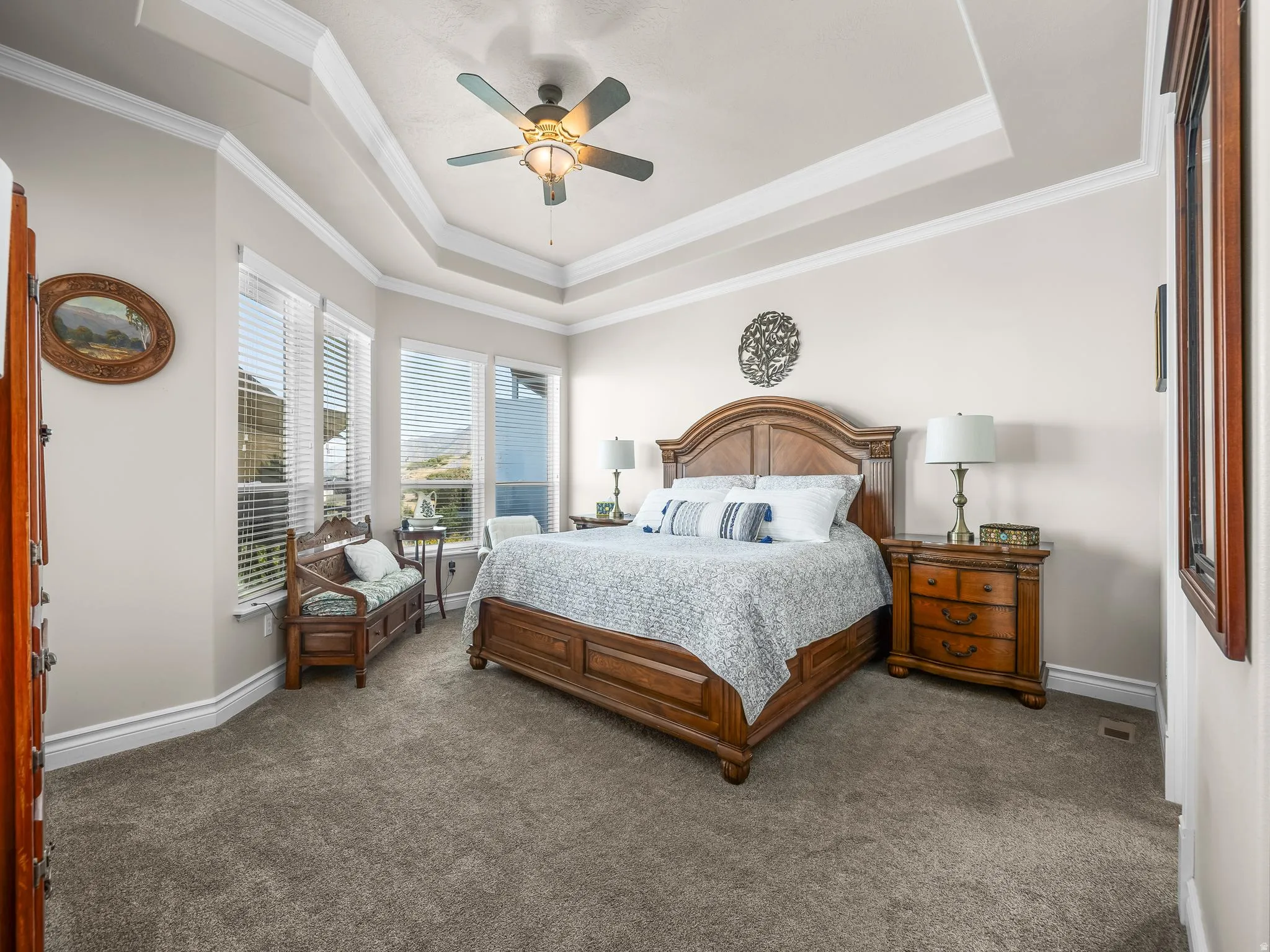Tray ceiling with crown molding, ceiling fan, and large windows with blinds
