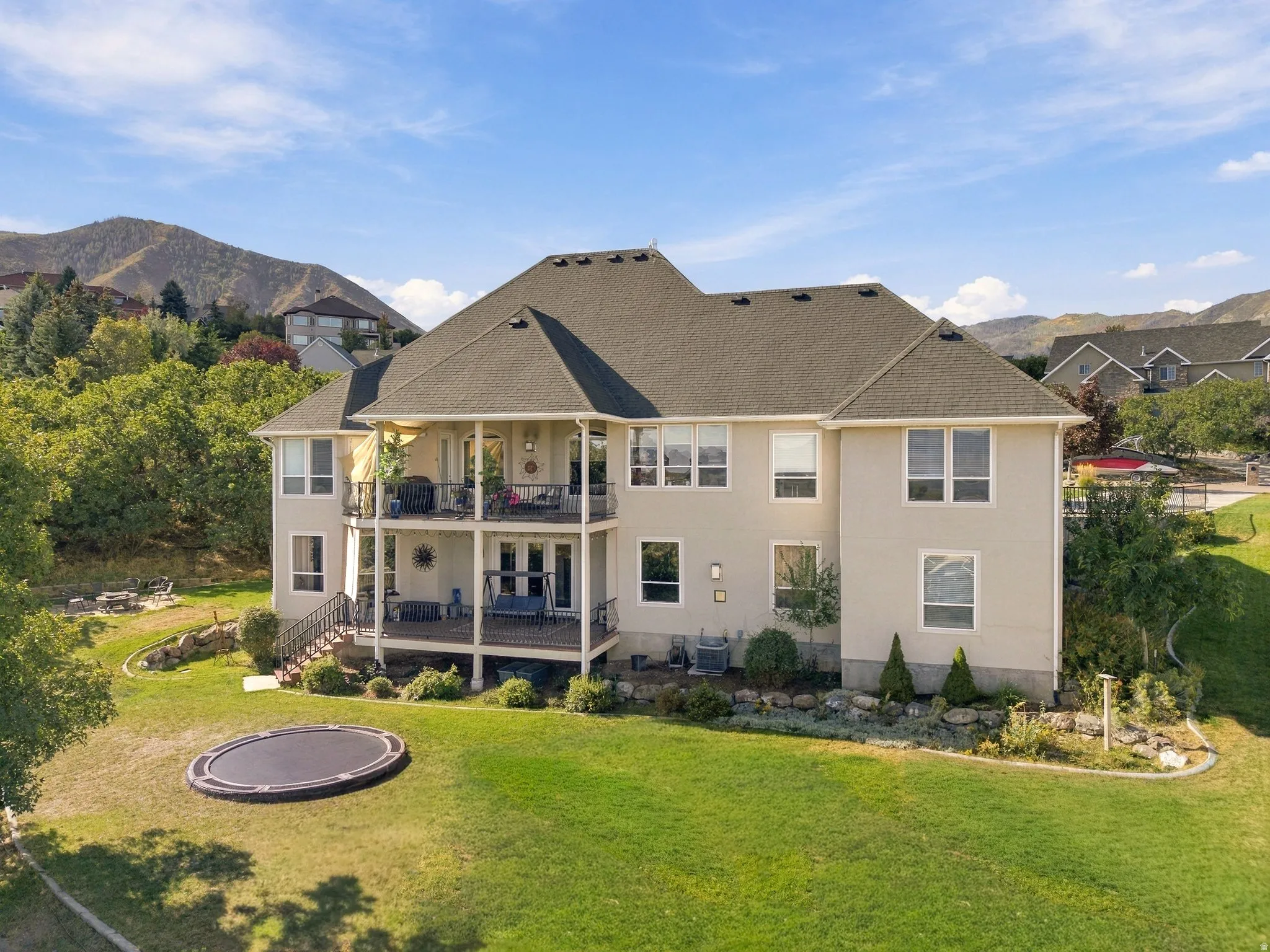 Expansive rear elevation featuring two covered balconies, a ground-level patio, and a terraced backyard with a manicured lawn