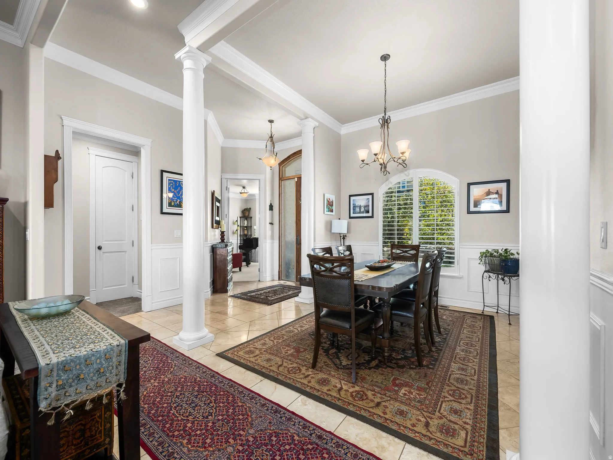 Tile flooring, wainscoting, decorative columns, arched window with plantation shutters, and crown molding
