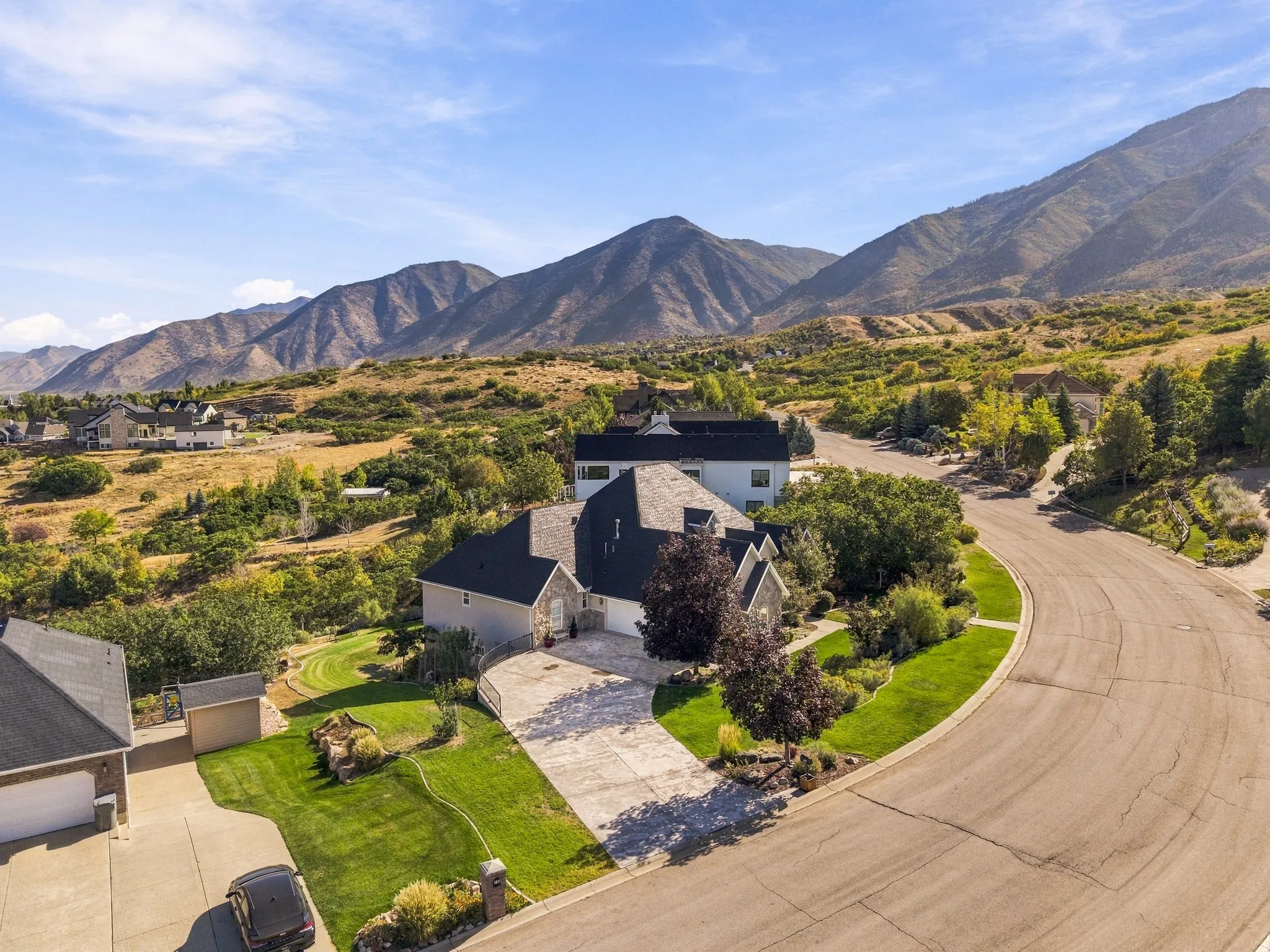 Expansive mountain backdrop, winding paved road, established landscaping, and a manicured lawn