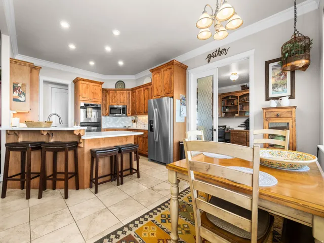 Kitchen featuring wood-finish cabinetry, stainless steel appliances, a white island with bar seating, recessed lighting, and tile flooring