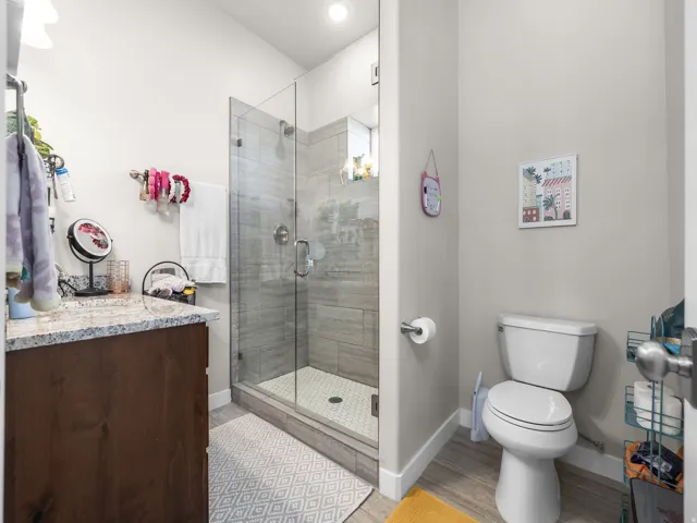 Glass-enclosed shower with tile surround and hexagonal floor tiles, wood-finish vanity with a speckled countertop, and modern commode