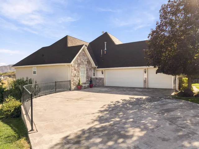 Stone facade accents, an arched entry doorway, a three-car garage, a concrete driveway, and an ornate metal railing