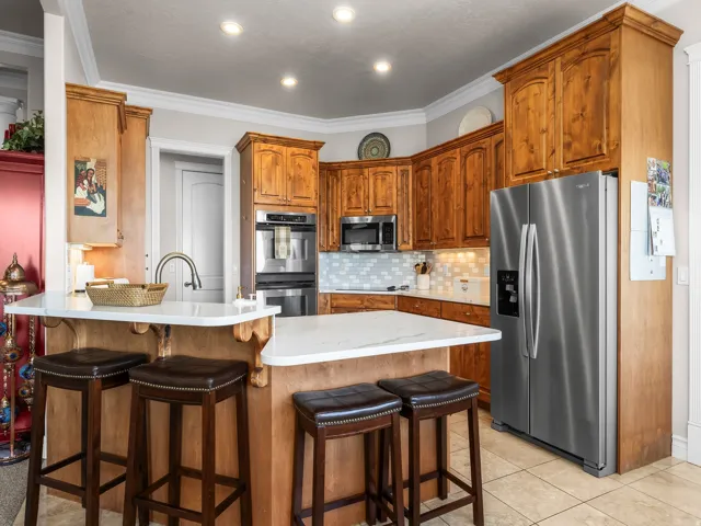 Kitchen featuring wood cabinetry, white countertops, tile flooring, stainless steel appliances, and a tile backsplash