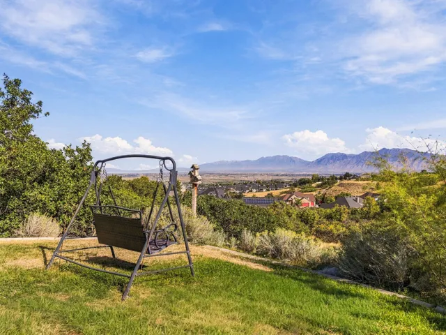 Expansive sloped lawn with mature landscaping, distant mountainous terrain, and a visible neighborhood below