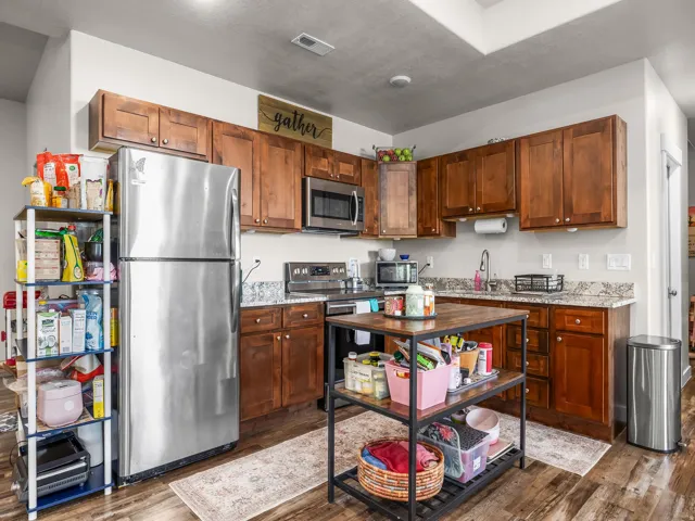 Kitchen featuring wood-finish flooring, stainless steel appliances, granite-style countertops, and rich wood cabinetry