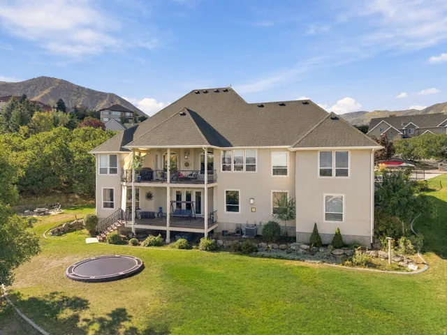 Expansive rear elevation featuring two covered balconies, a ground-level patio, and a terraced backyard with a manicured lawn