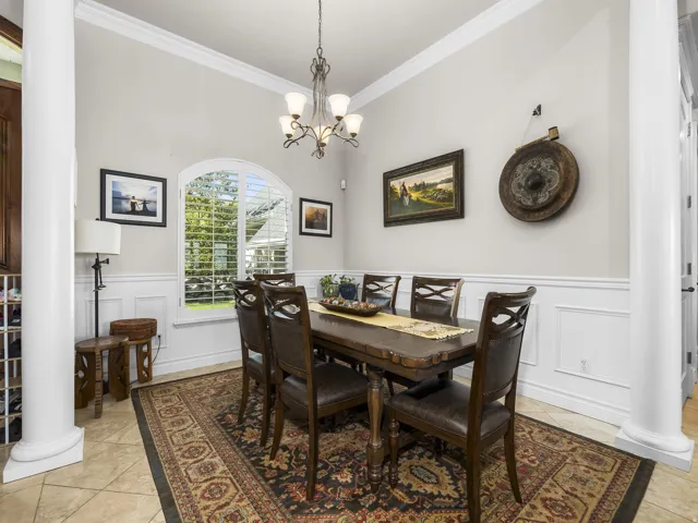 Arched window with plantation shutters, decorative wainscoting, crown molding, and tiled flooring