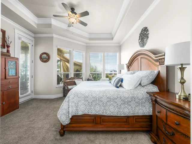 Recessed tray ceiling with a ceiling fan, bay window with multiple panes, carpeted flooring, and a glass-paneled door