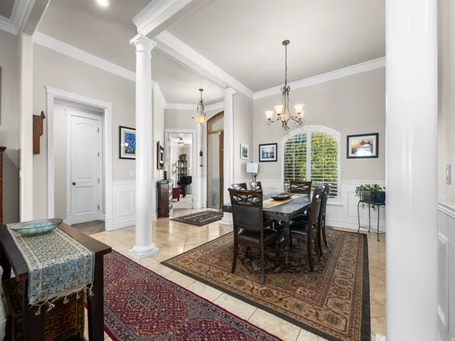 Tile flooring, wainscoting, decorative columns, arched window with plantation shutters, and crown molding
