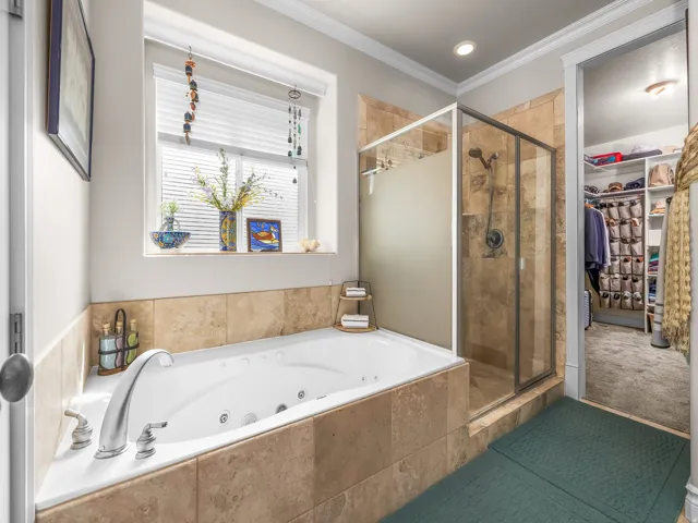 Jetted soaking tub with tile surround, glass-enclosed shower, and built-in closet system