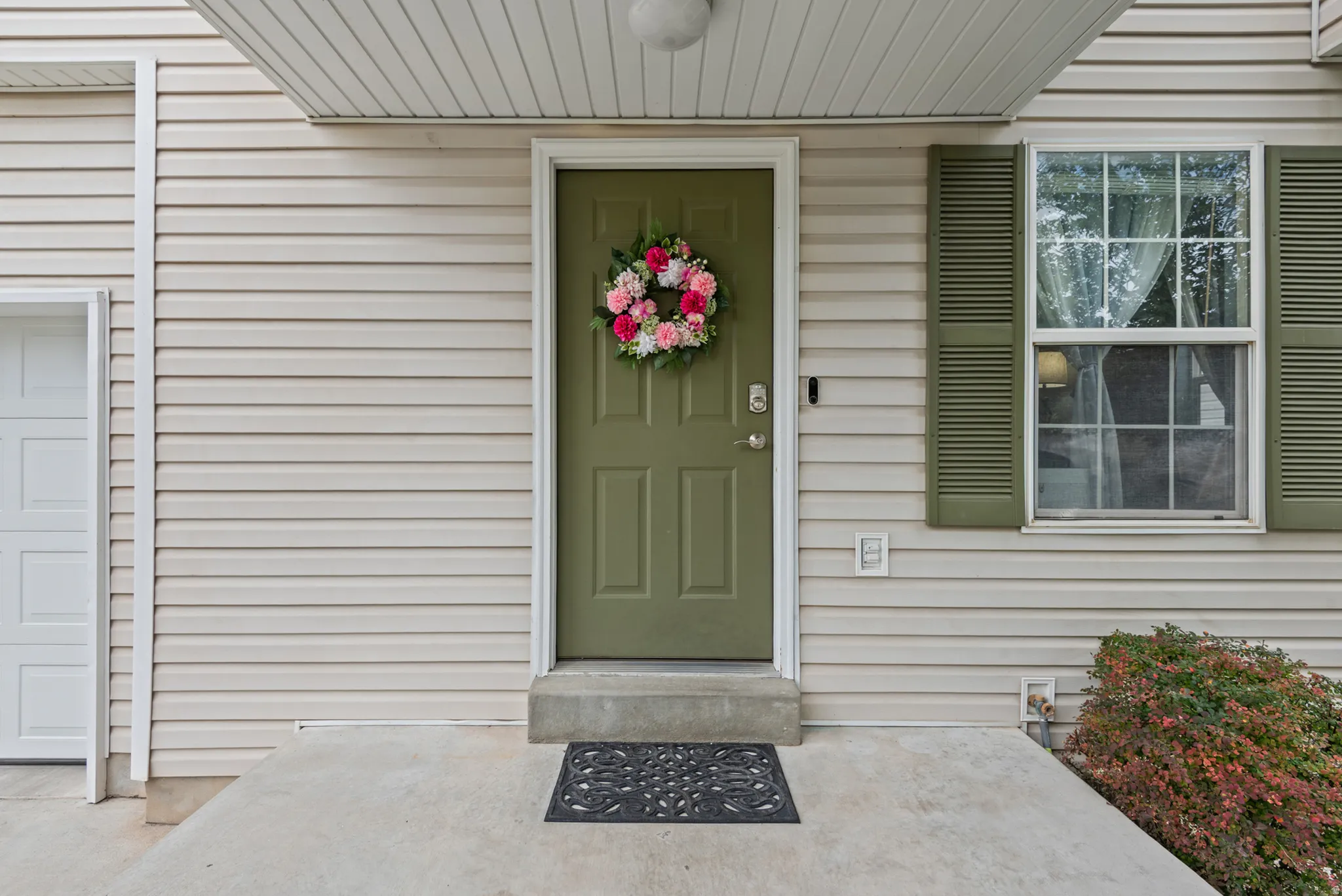 Light-colored siding exterior with a green panel entry door, a single-pane window with green louvered shutters, and a concrete entry porch
