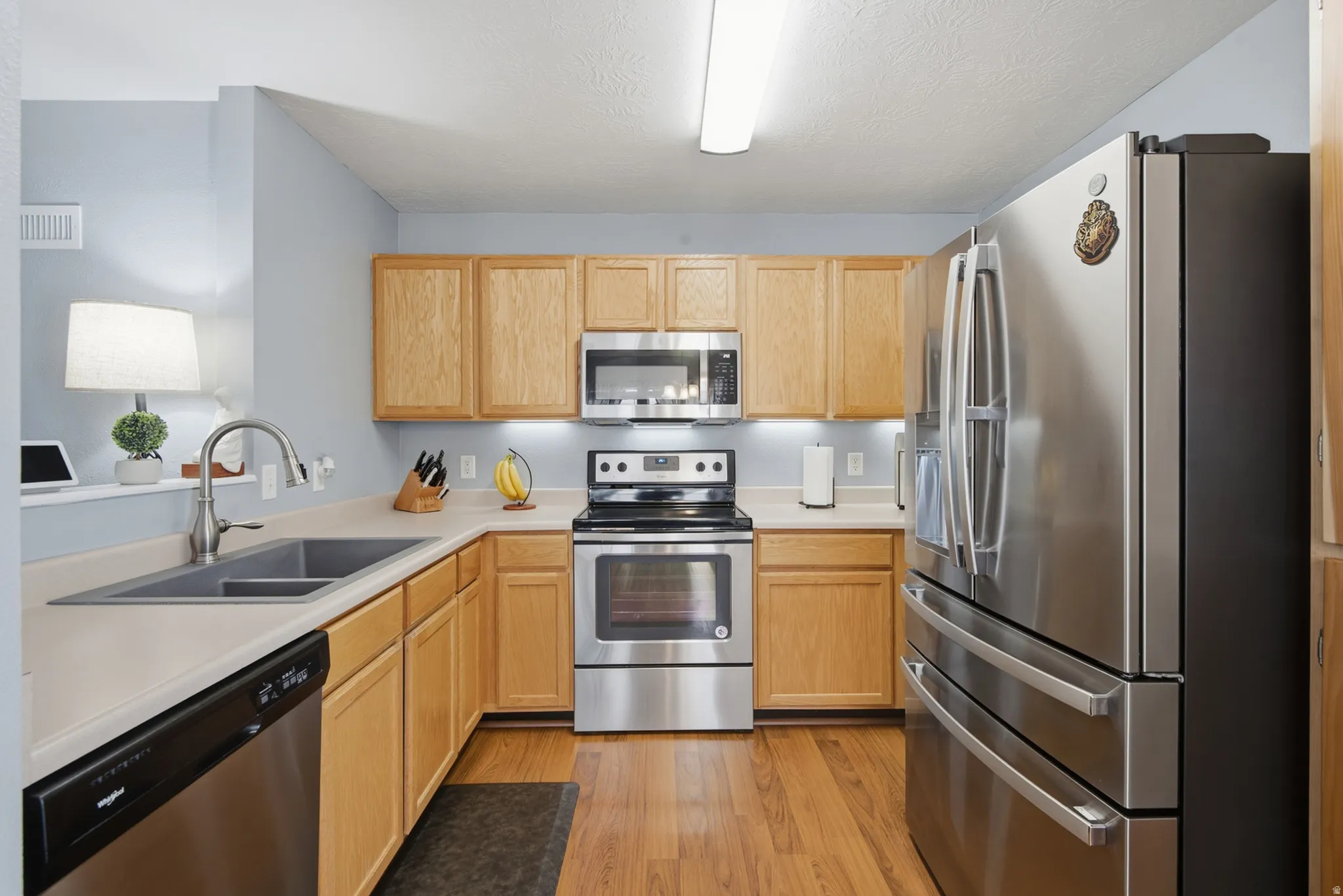 Stainless steel appliances, wood-finish flooring, wood cabinetry, built-in microwave, and an undermount sink