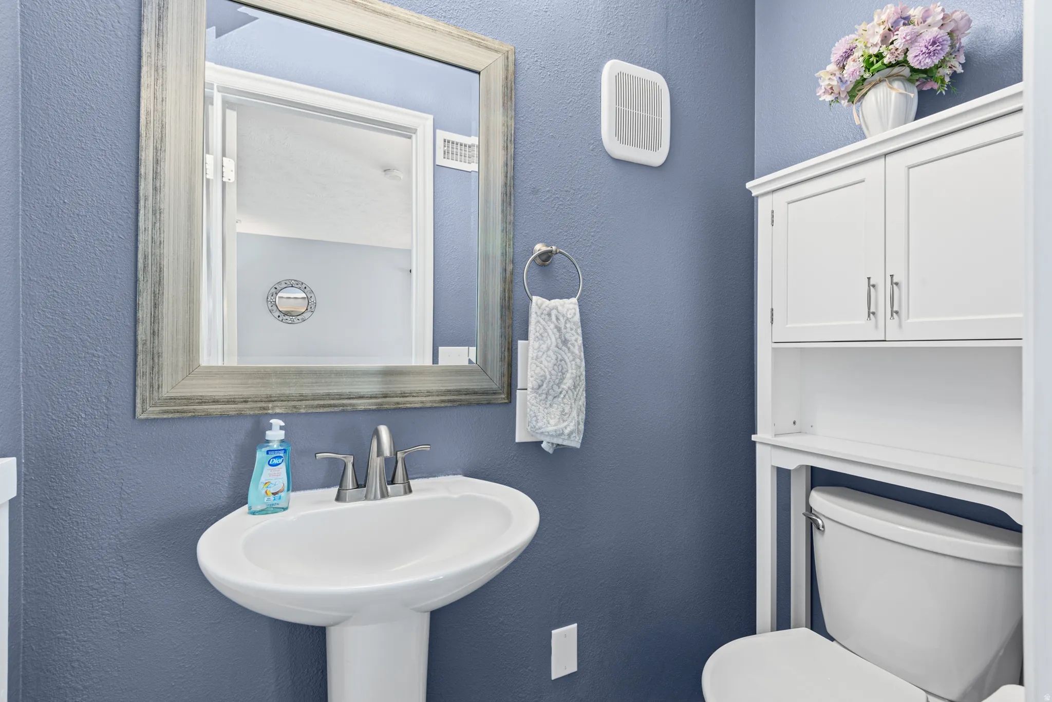 Pedestal sink with a polished chrome faucet, framed mirror, and an over-the-toilet storage cabinet