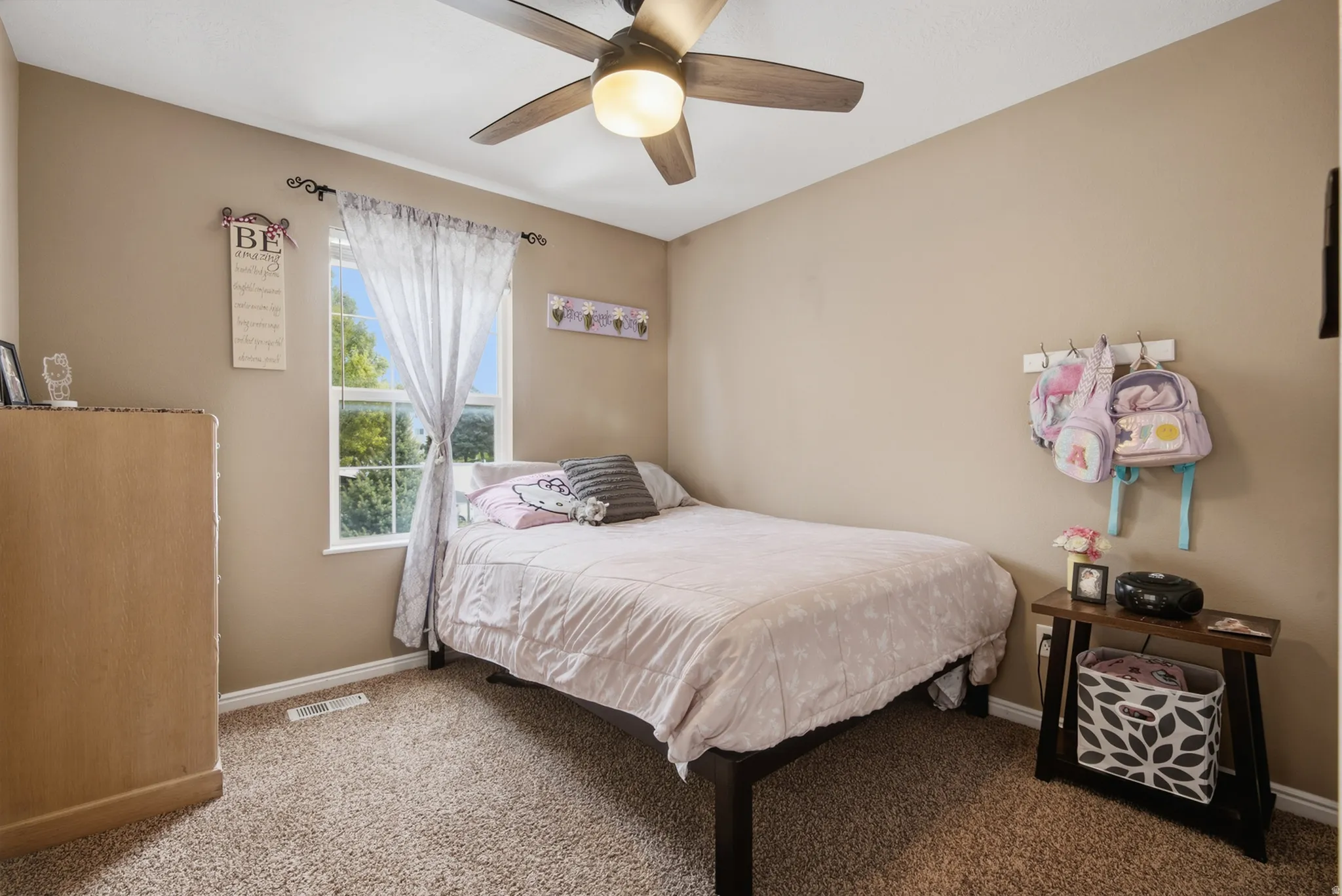 Plush carpet flooring, a ceiling fan with integrated lighting, and a window providing natural light
